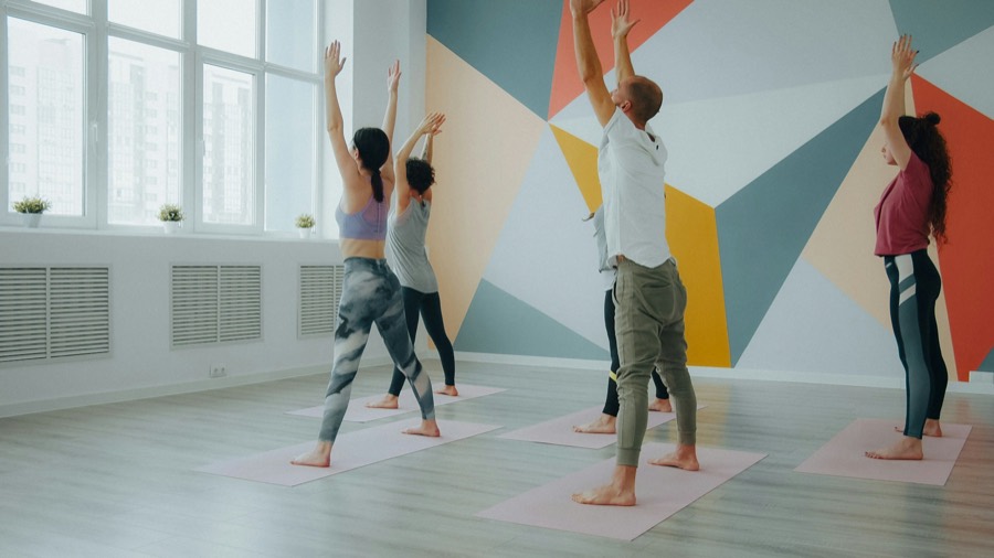 Un cours de yoga, bras levés, dans un studio coloré